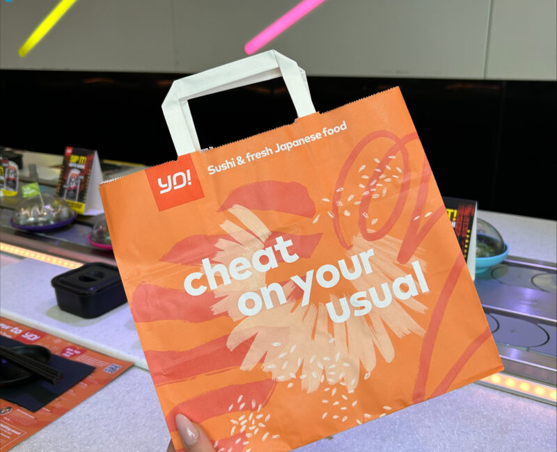 Someone holding up a Yo Sushi takeaway bag inside the Yo Sushi restaurant at Manchester Arndale
