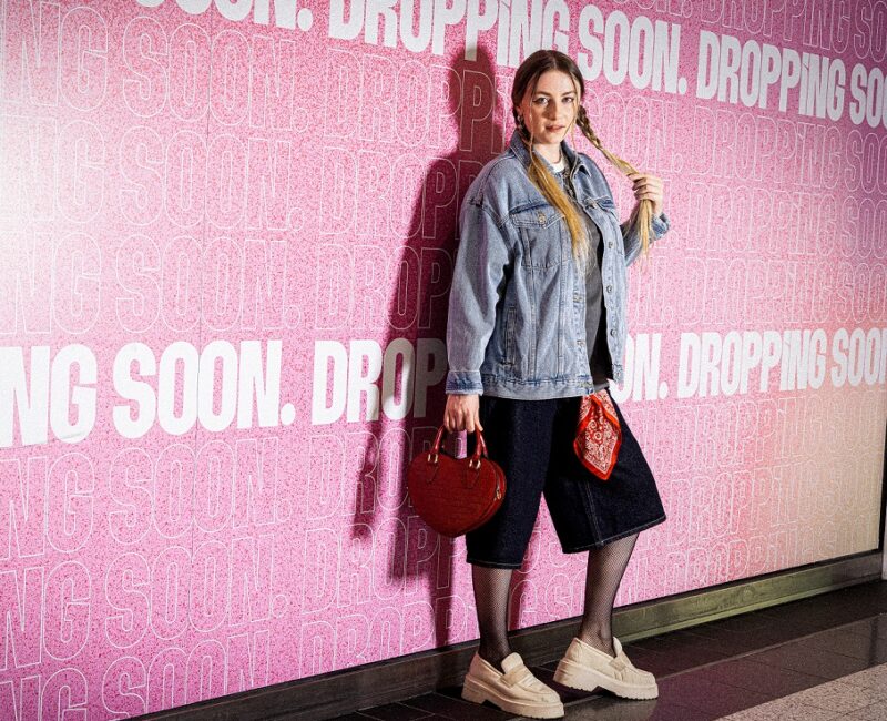 Girl wearing double denim leaning against a pink wall