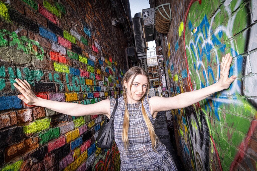 Woman standing between two walls covered in art and graffiti.